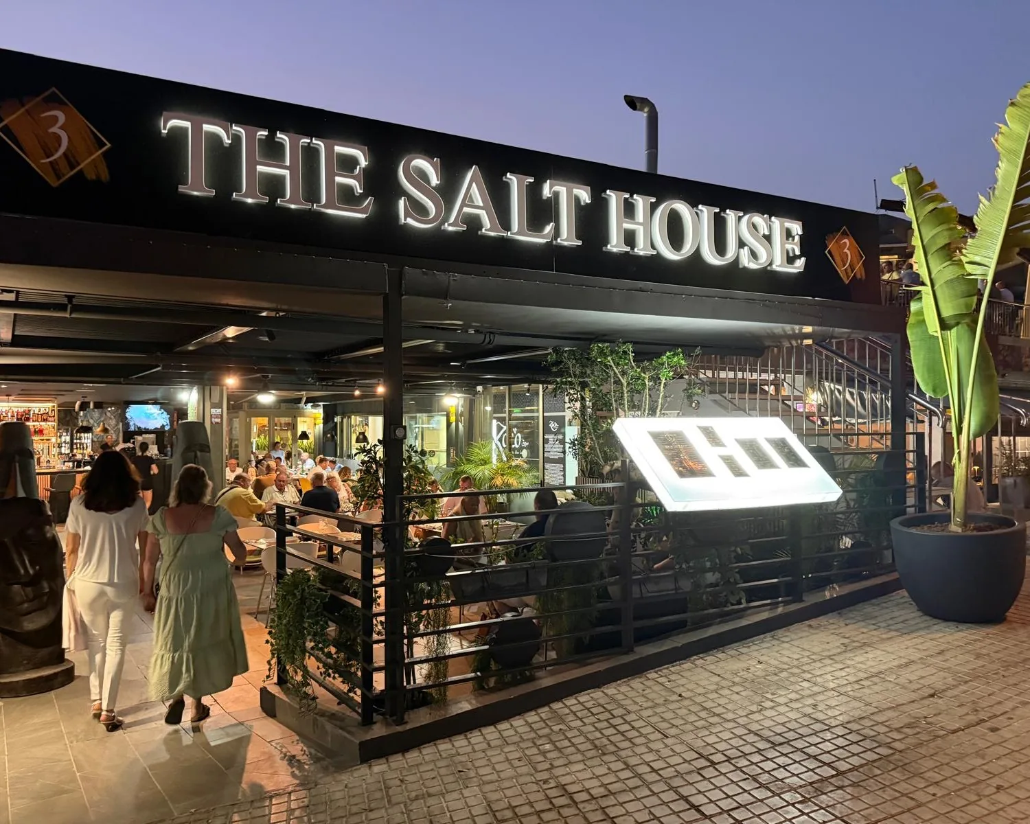 Gäste betreten The Salt House in der Abenddämmerung, unter dem beleuchteten Schild