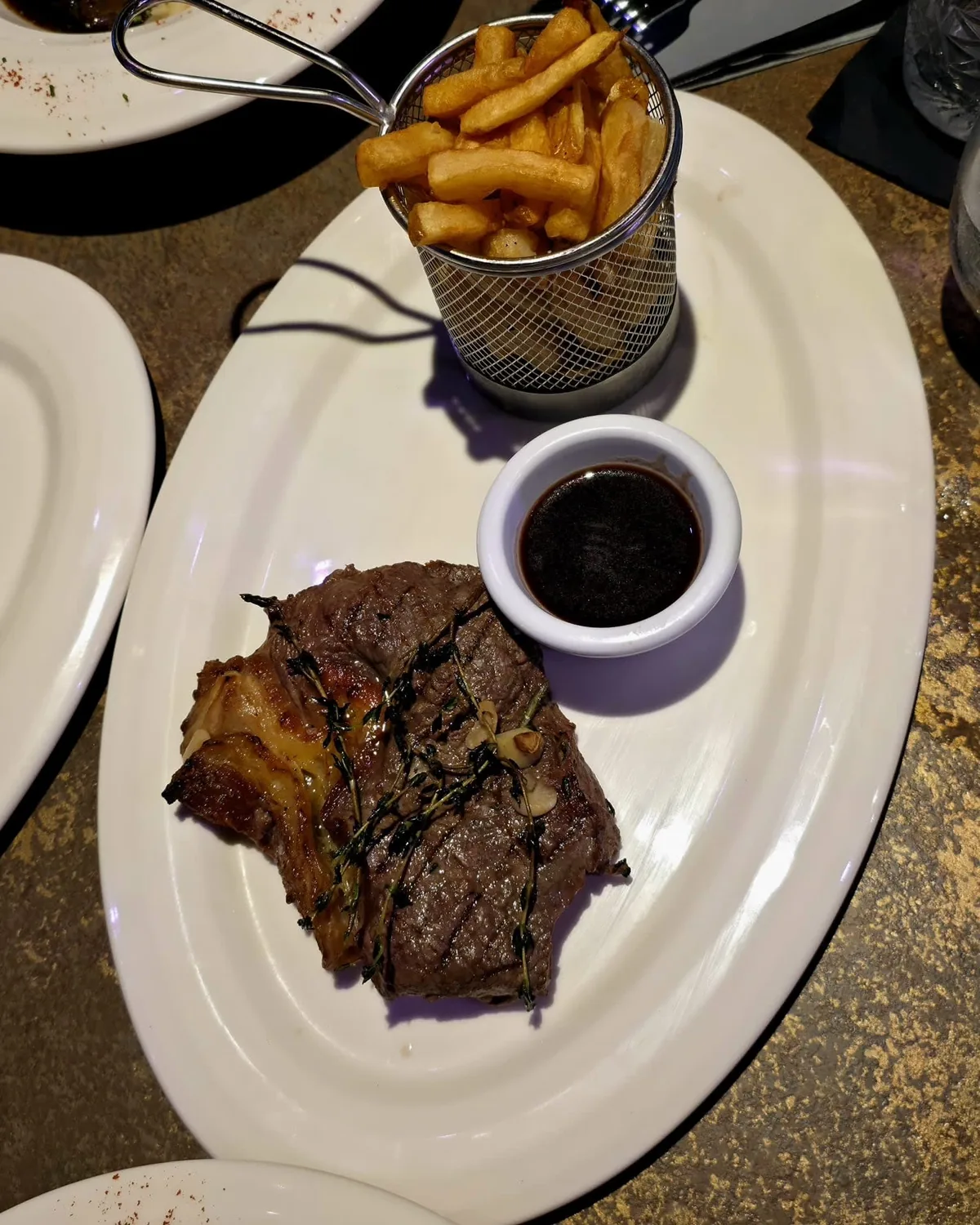 Ein gegrilltes Steak mit einem Sch&auml;lchen Sauce und einem K&ouml;rbchen Pommes