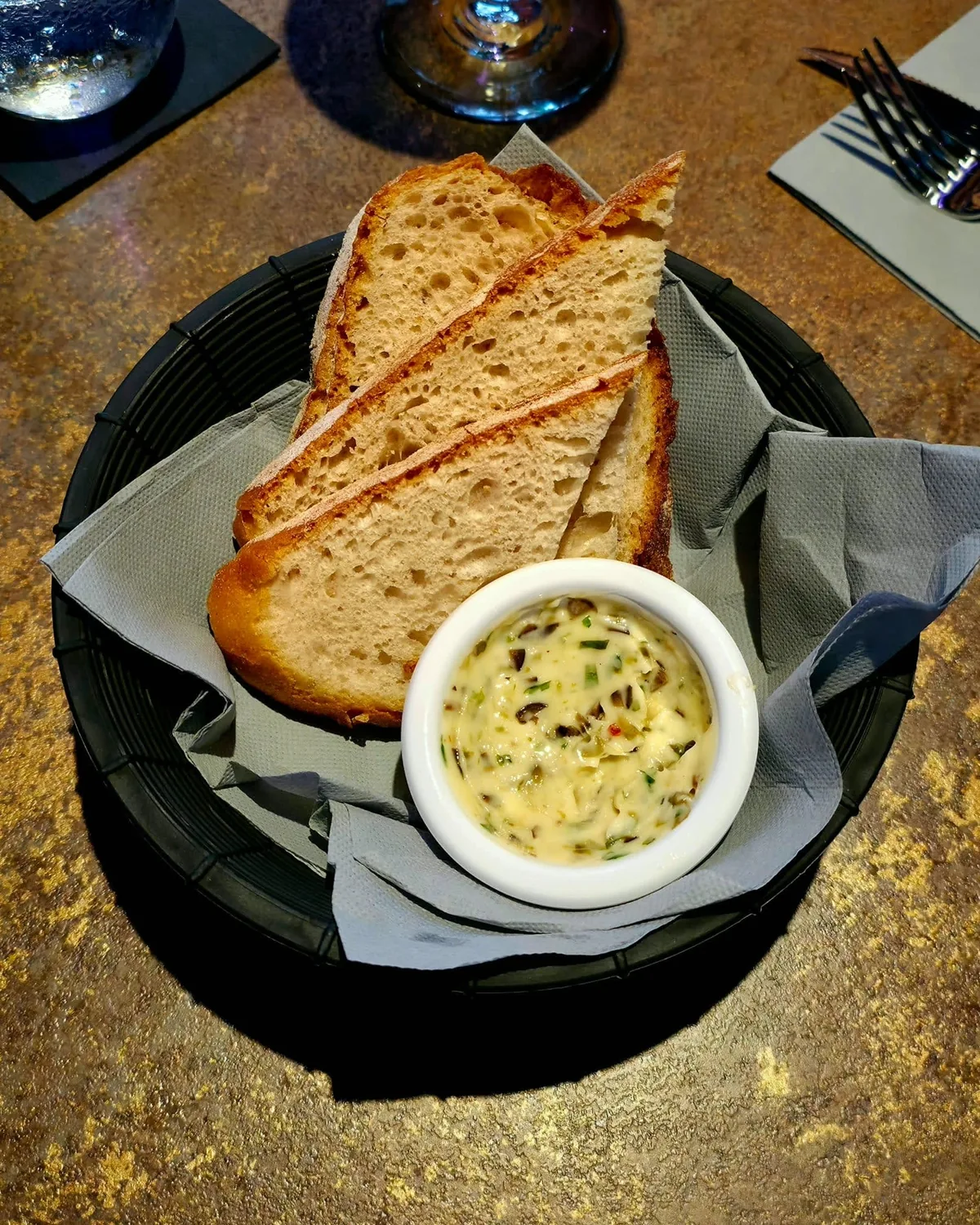 Sauerteigbrot in Scheiben in einem Korb mit Papier, dazu ein Sch&auml;lchen Butter mit Oliven und Kr&auml;utern