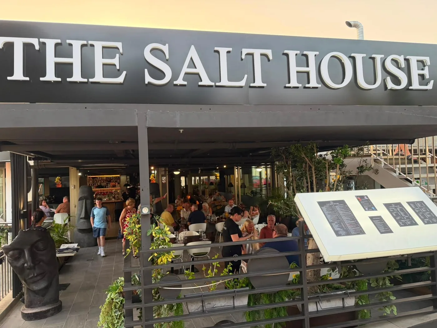 Diners on the terrace at dusk, under the big The Salt House sign