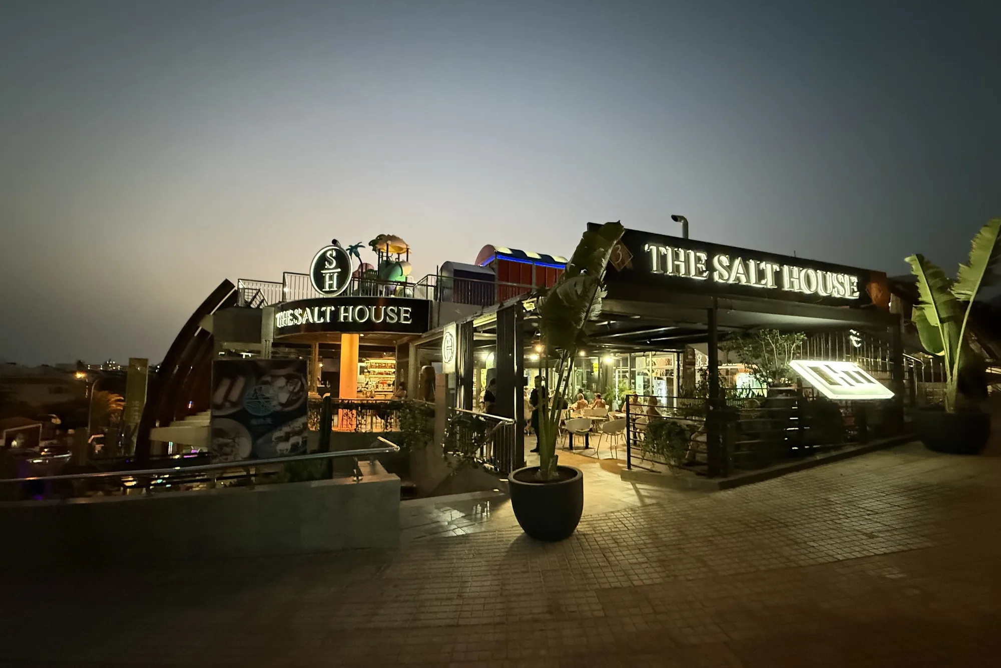 The Salt House at night: the lit sign, the terrace and the plants along the front